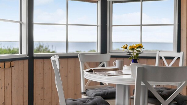 A covered patio with a table and chairs, a vase with yellow flowers, and a view of the sea. - 2 bedroom cozy home in Esbjerg V (Esbjerg V)