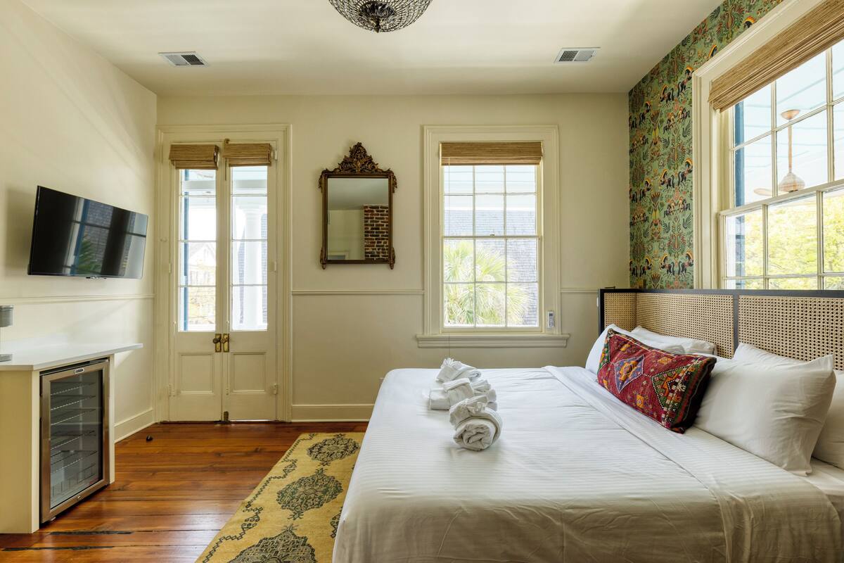 A hotel room with a bed, a television, a mirror, and two windows.