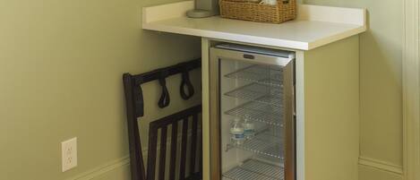 Una pequeña kitchenette con refrigerador, microondas y lavamanos. Hay cuadros en la pared y un televisor de pantalla plana montado sobre la encimera.