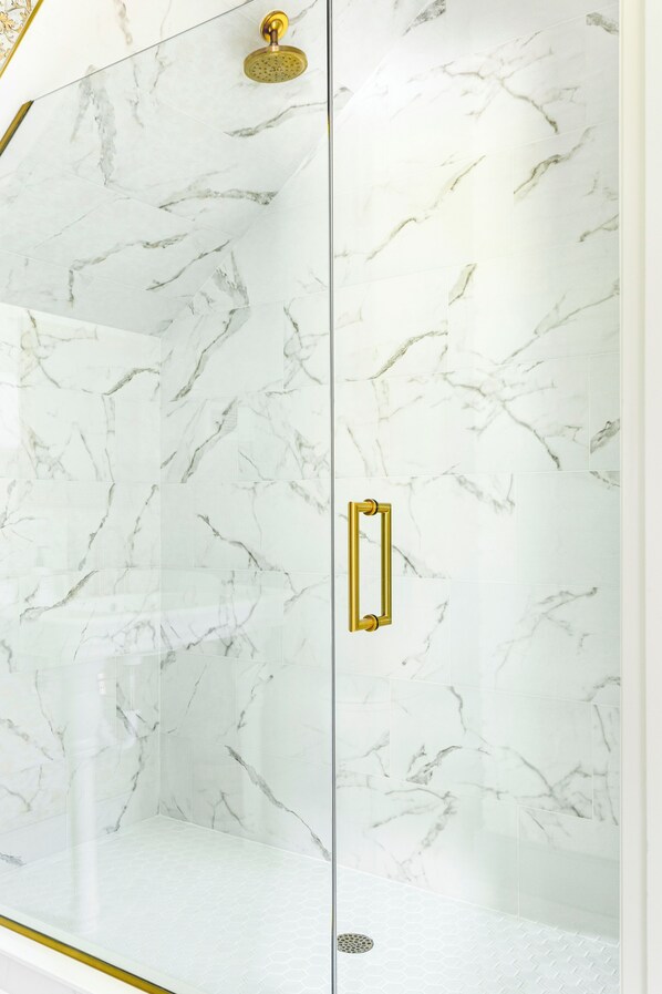 A glass-enclosed shower with marble walls and a gold handle. - The Ashley (Charleston)