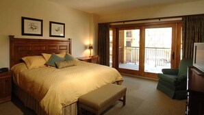 A hotel room with a large bed, a bench, a television, a desk, and a balcony with a view. - Mtn View King Room | Swimming Pool + Gym (Crested Butte)