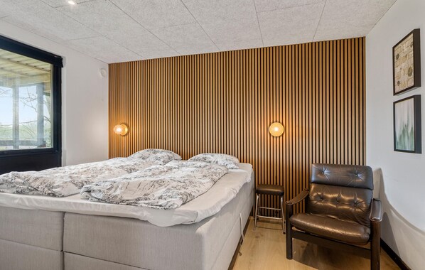 Un dormitorio con una cama, una silla y una pared con listones de madera verticales.