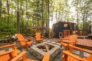 A cabin with a deck, outdoor seating, and a fire pit surrounded by a forest. - Rustic Charm Meets Modern Boutique + Lake Central + Hot Tub, Sauna, Lake Access (Oakland)
