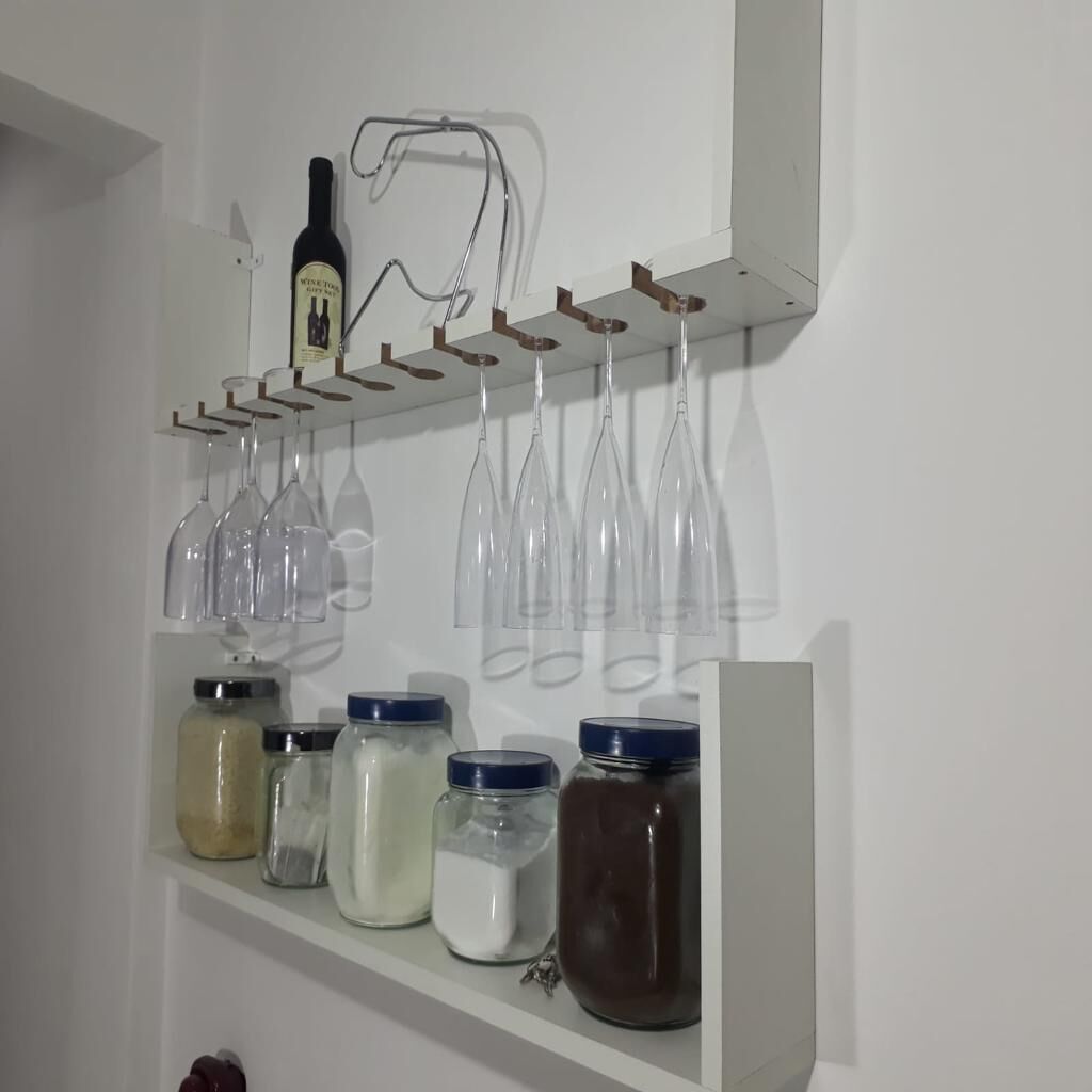 A kitchen shelf with wine bottles, glasses, and jars of spices.