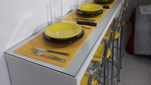 A dining area with a long table set with yellow plates, clear glasses, and cutlery. - Studio Central Próximo a Rodoviária (Curitiba)