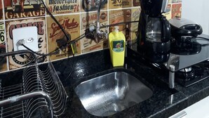 A kitchen with a black countertop, a coffee maker, and a wall with vintage automotive-themed tiles. - Studio Central Próximo a Rodoviária (Curitiba)