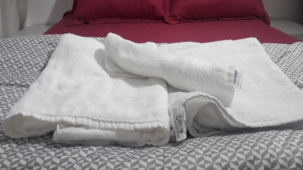 A bed with a geometric patterned bedspread, two red pillows, and a folded white towel on the bed. - Studio Central Próximo a Rodoviária (Curitiba)