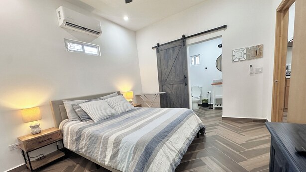 A bedroom with a bed, nightstand, lamp, and a sliding barn door leading to a bathroom. - Relax in Style at Depa Azul in Puerto Peñasco (Puerto Peñasco)