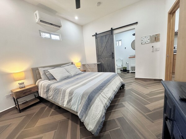 A bedroom with a bed, nightstand, lamp, and a sliding barn door leading to a bathroom. - Relax in Style at Depa Azul in Puerto Peñasco (Puerto Peñasco)