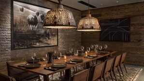 A dining area with a long wooden table set for six, two hanging pendant lights, a large framed picture of cattle, and a geometric wall design. - 4 Bedroom Luxury Residence at World-class Resort in Lionshead Village (Vail)