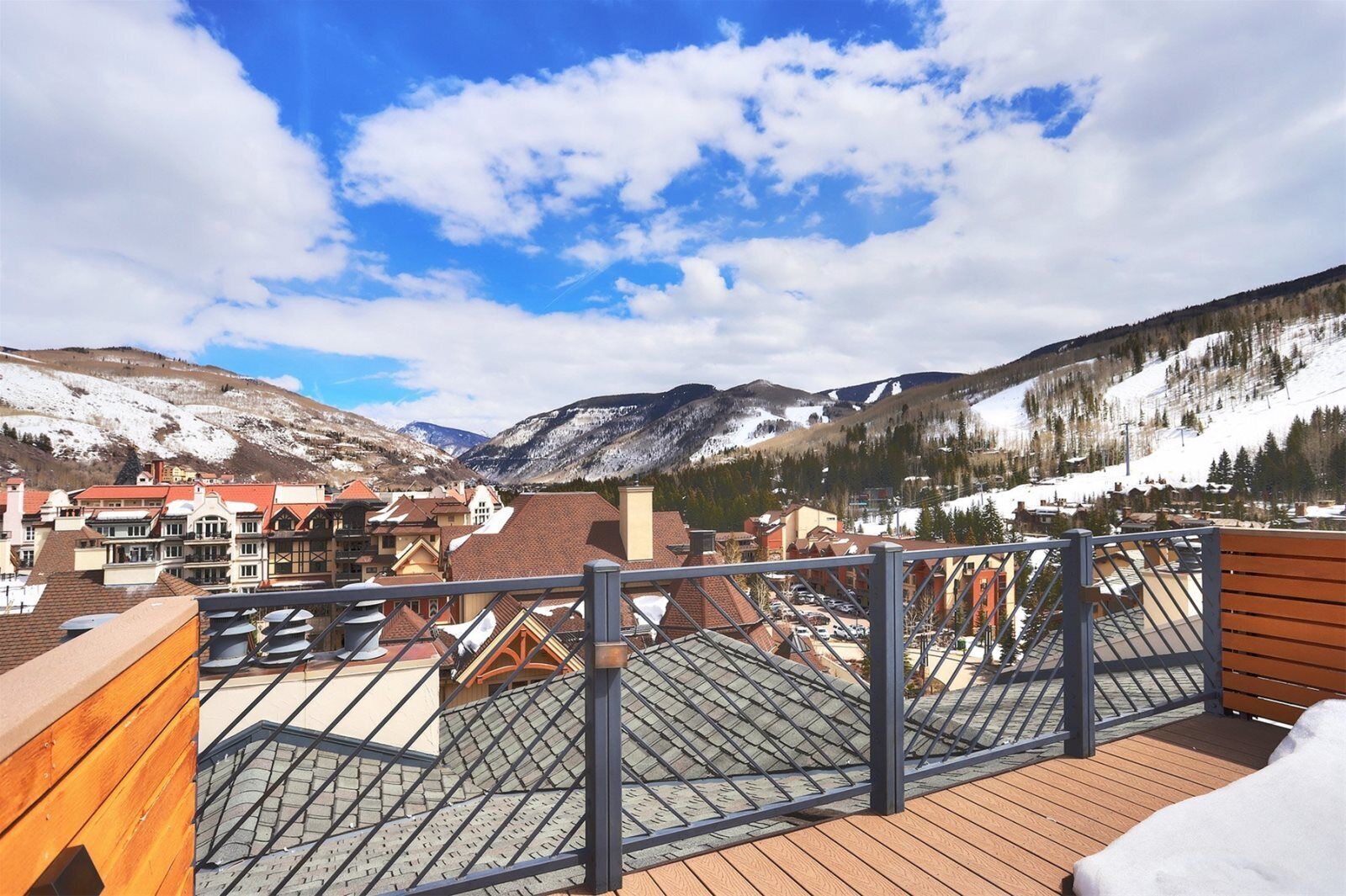 Une terrasse sur le toit offrant une vue sur un paysage montagneux, avec des rampes en bois et un sol recouvert de neige.