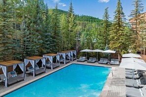 A pool area with lounge chairs and umbrellas, surrounded by tall trees. - 4 Bedroom Luxury Residence at World-class Resort in Lionshead Village (Vail)