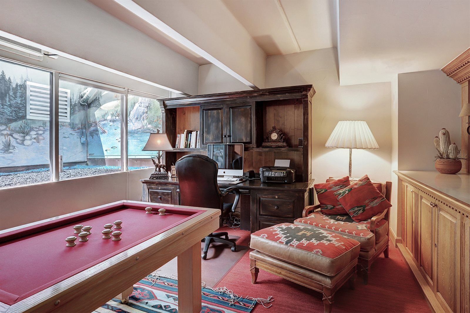 A cozy room with a pool table, a comfortable sofa, a desk with a computer, and a bookshelf.