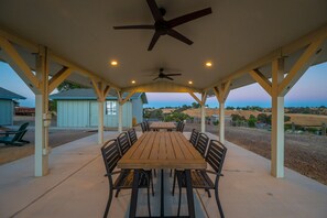 An outdoor covered patio with a wooden table and chairs, ceiling fans, and a view of the countryside. - Wine Country Escape*Hot Tub*Fire Pit (Paso Robles)