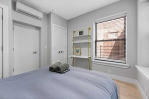 Relax in a serene bedroom with a large bed, bedside table, and window with blinds.