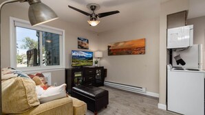 A compact living space with a sofa, a television, a ceiling fan, and a refrigerator.