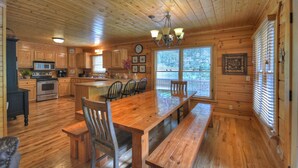 A wooden cabin interior with a kitchen, dining area, and a large wooden table.