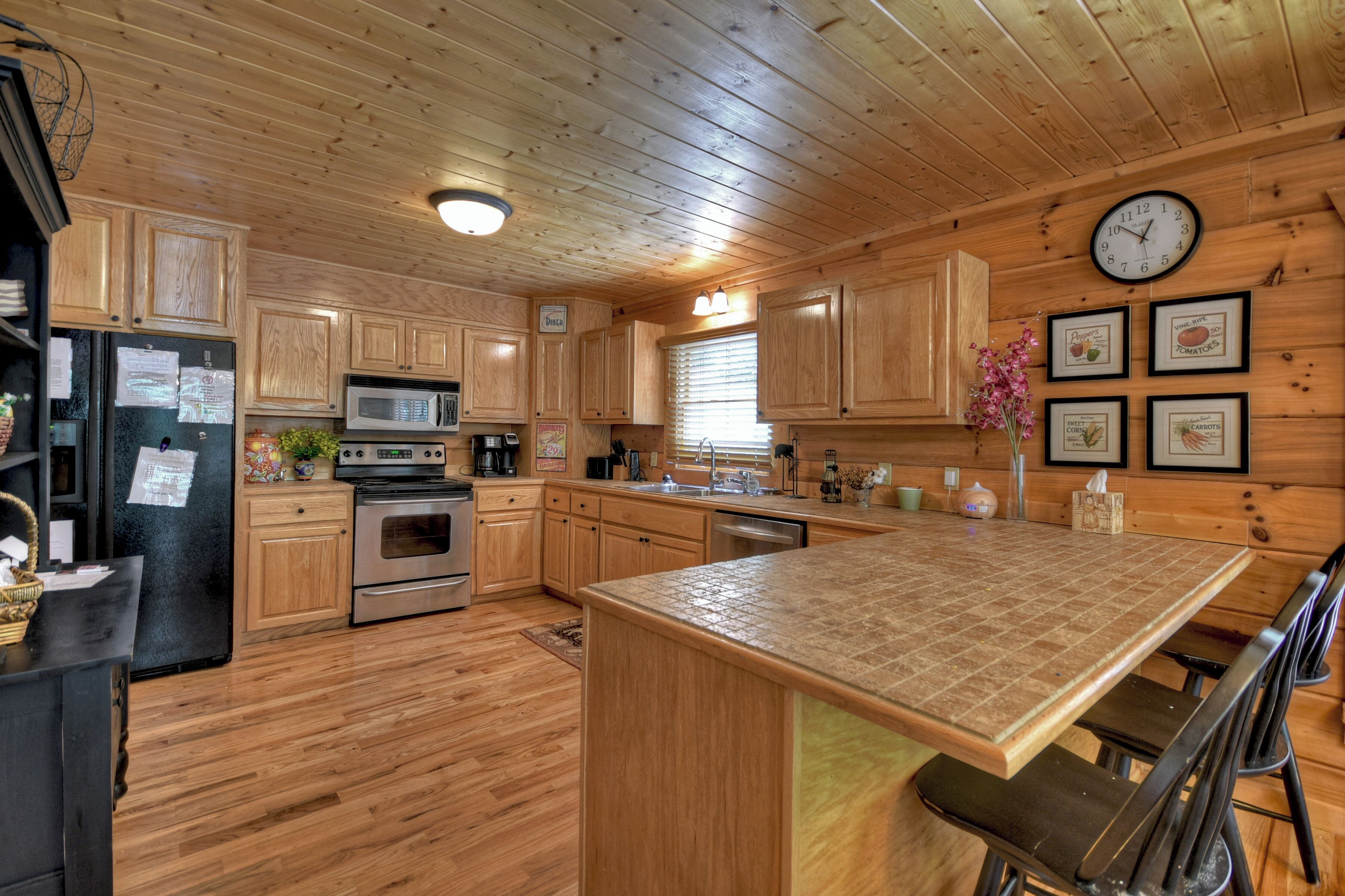 A wooden cabin-style kitchen with wooden cabinets, a microwave, an oven, a sink, and a clock on the wall.