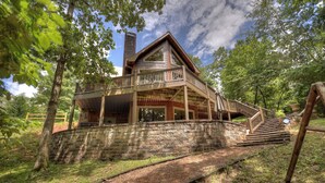 A rustic cabin with a wooden deck and a stone retaining wall.