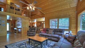 A spacious living room with a high ceiling, wooden walls, and a large window.