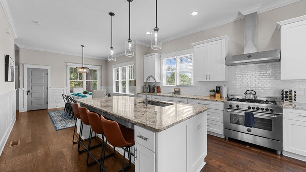 A modern kitchen with white cabinetry, a large island with bar stools, stainless steel appliances, and pendant lighting. - Traditional 4BR Craftsman, In DT Durham, Near Duke (Durham)
