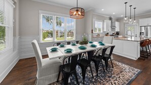 A modern kitchen with white cabinetry, a dining table set with teal plates, and a large window offering a view of the city. - Traditional 4BR Craftsman, In DT Durham, Near Duke (Durham)