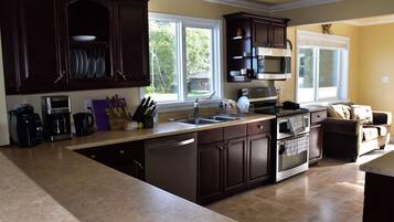 A modern kitchen with dark wood cabinets, a large island with a sink, and a built-in oven. There are windows providing natural light and a view of the outdoors.