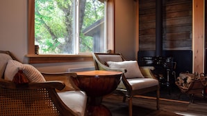 Une pièce chaleureuse avec des fauteuils en osier, une table ronde en bois et une grande fenêtre donnant sur les arbres.