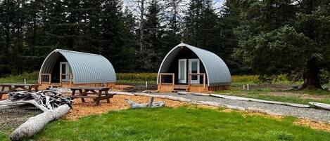 Two dome-shaped cabins with wooden decks, surrounded by a forest.