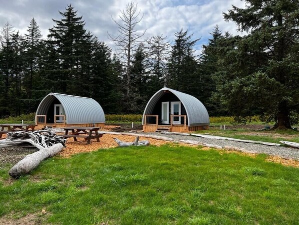 Deux cabanes en forme de dôme, dotées de terrasses en bois, et entourées d’une forêt.