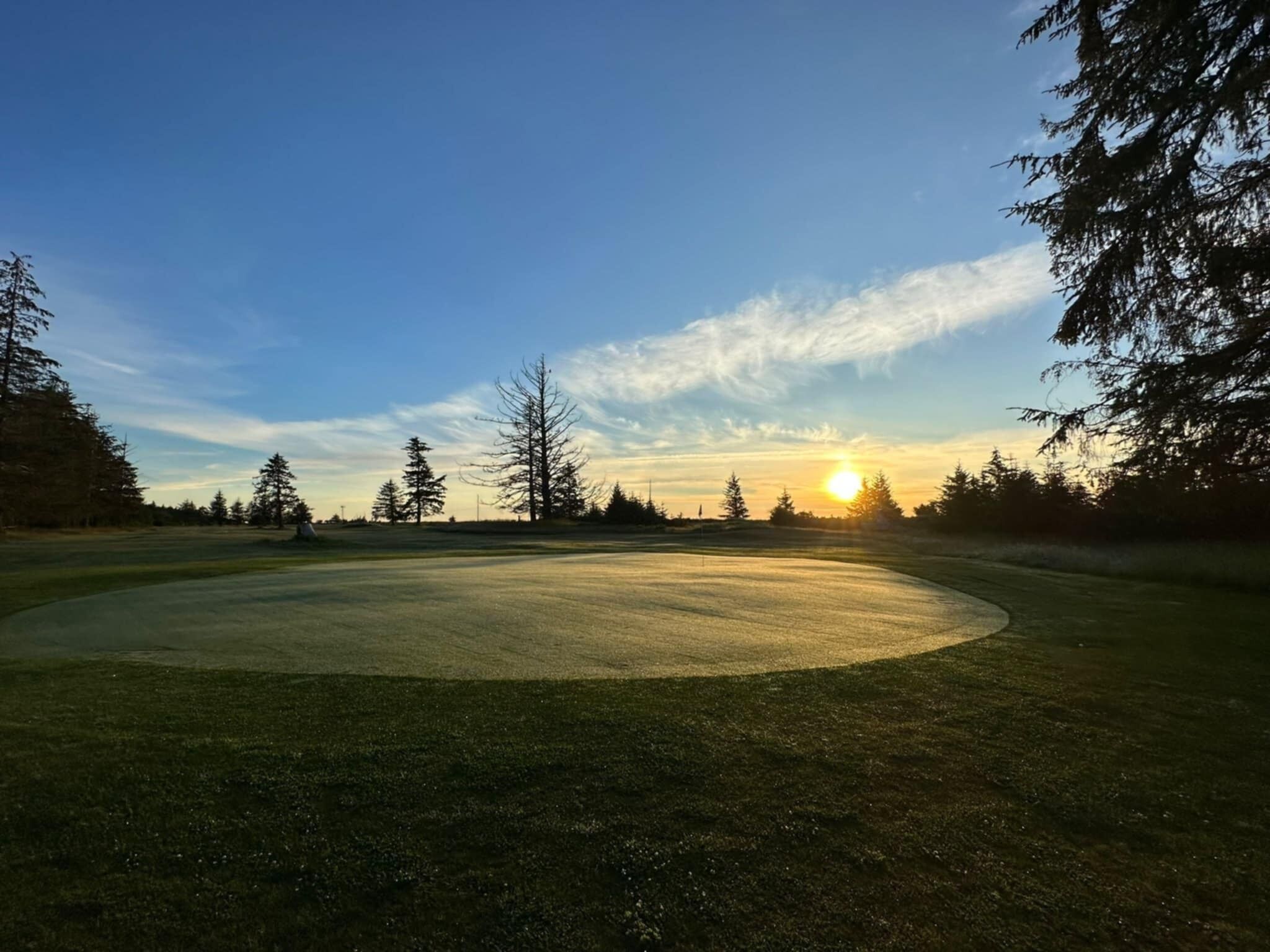A golf course with a clear sky and a sunset in the background.
