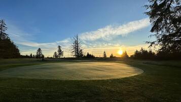 A golf course with a clear sky and a sunset in the background.