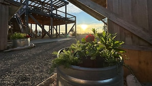 Un espace extérieur abrité doté d’une structure en bois, d’un jardinière en métal contenant des plantes et, en arrière-plan, un coucher de soleil.