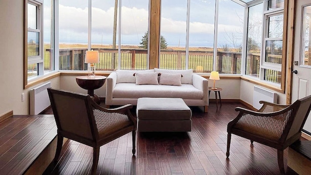 Une pièce chaleureuse avec une grande fenêtre en verre, un canapé, deux fauteuils et une lampe.