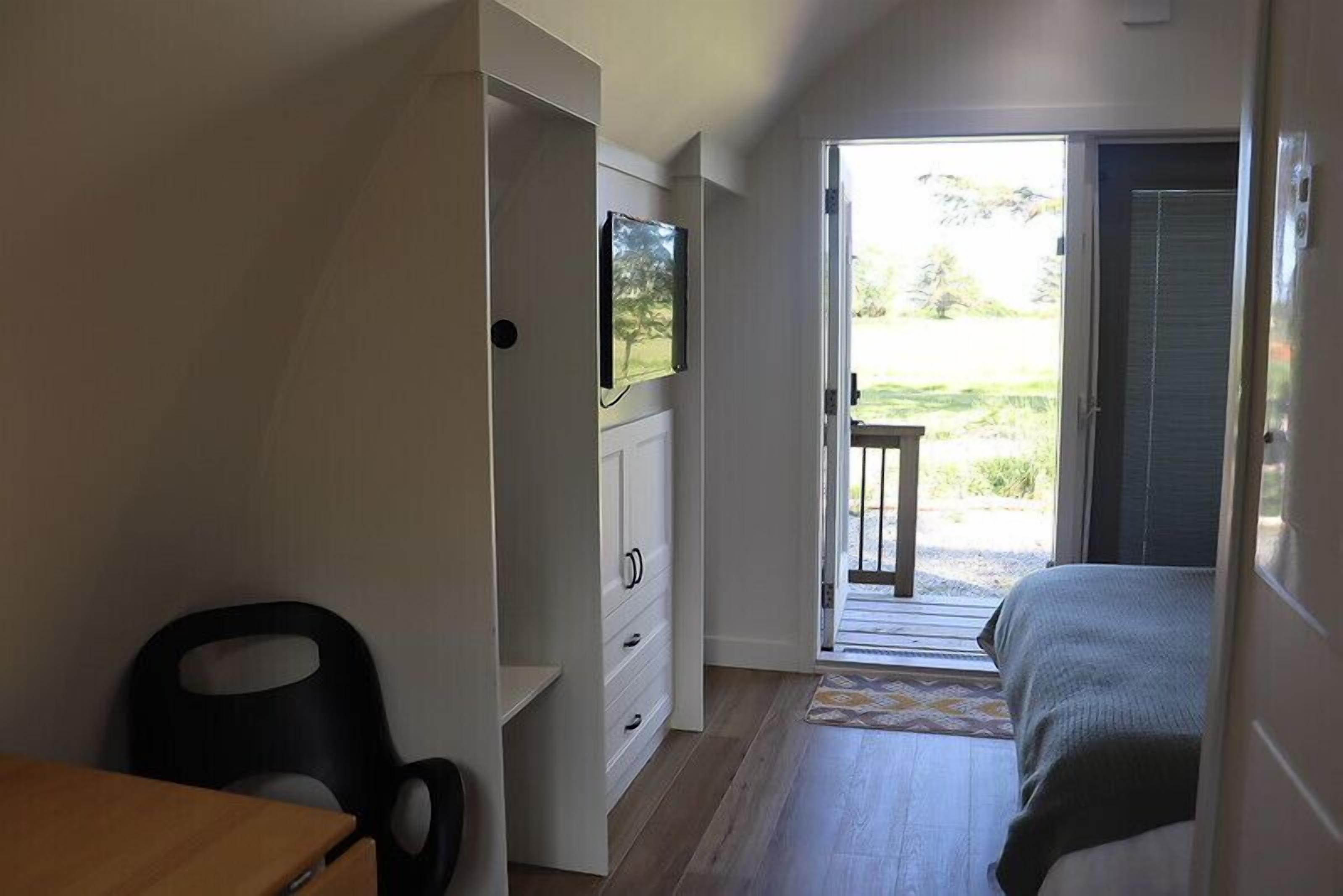 Quarto com cama, escrivaninha, cadeira, televisão e porta deslizante que dá para uma varanda.