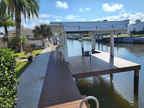 A wooden dock extending over a calm body of water, with a covered seating area and chairs. - Intercostal channel house with boat dock and ping-pong table (South Daytona)