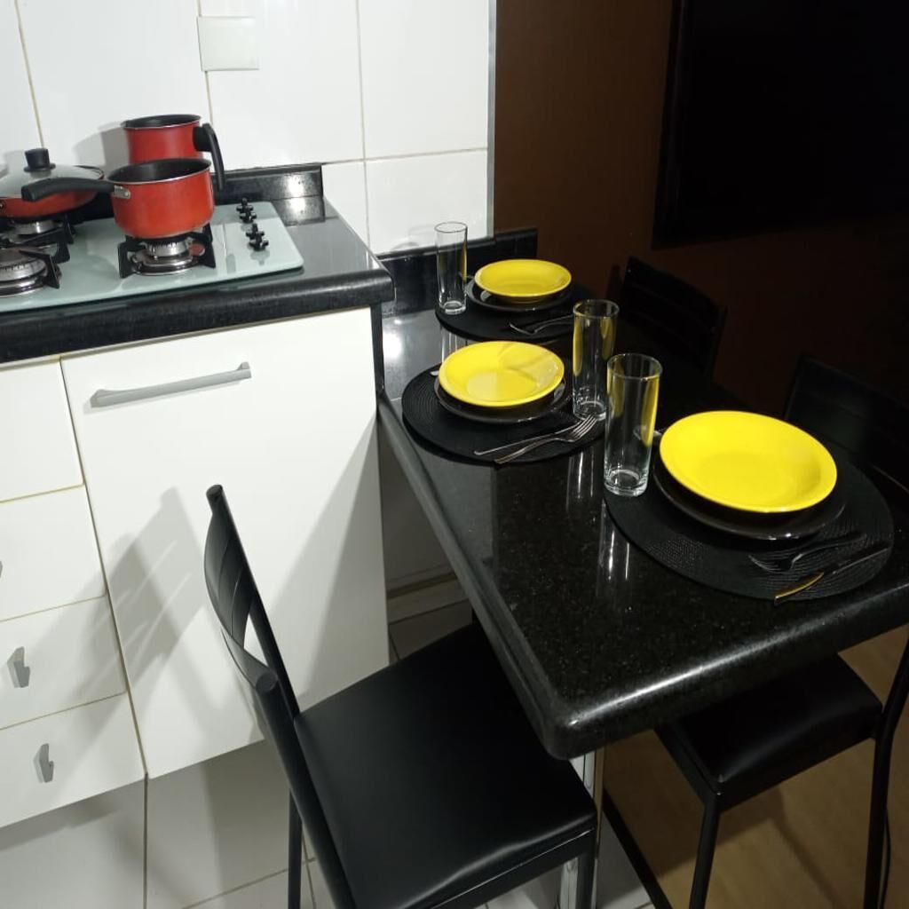 Une cuisine équipée d’une cuisinière, de casseroles et d’une table à manger dressée avec des assiettes, des verres et des couverts jaunes.