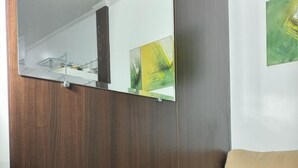 Une pièce comprenant une armoire en bois, un canapé beige et un miroir qui reflète une peinture abstraite aux tons verts.
