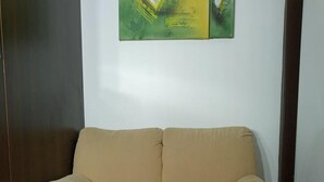 Un canapé beige avec des accoudoirs, dans une pièce dotée d’une porte en bois foncé et d’un mur blanc.