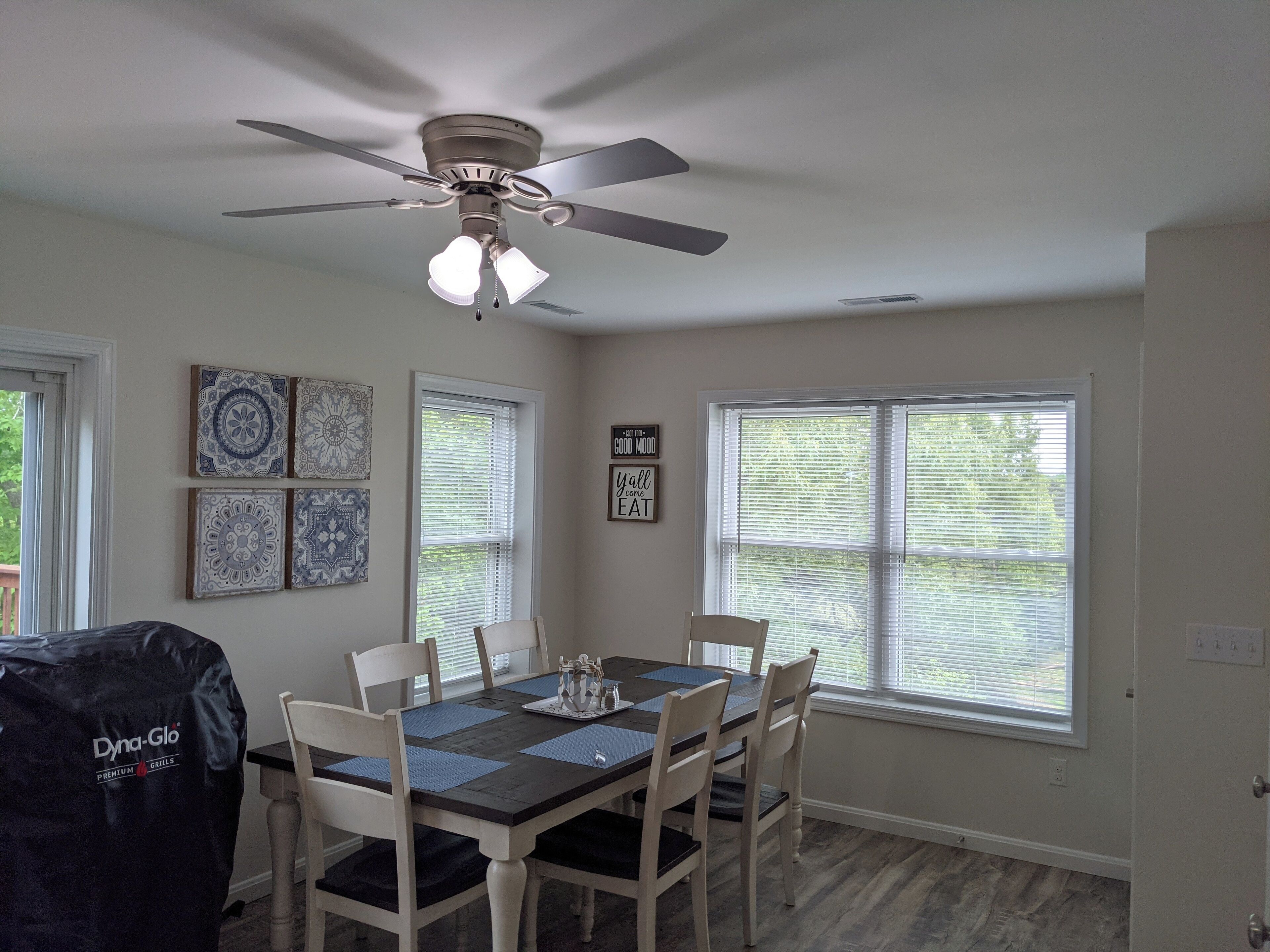 Un coin repas avec une table dressée pour quatre personnes, un ventilateur de plafond et des œuvres d’art décoratives accrochées au mur.