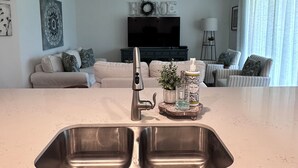 A modern kitchen with a stainless steel sink, a built-in oven, and a dining area with a sofa and chairs.
