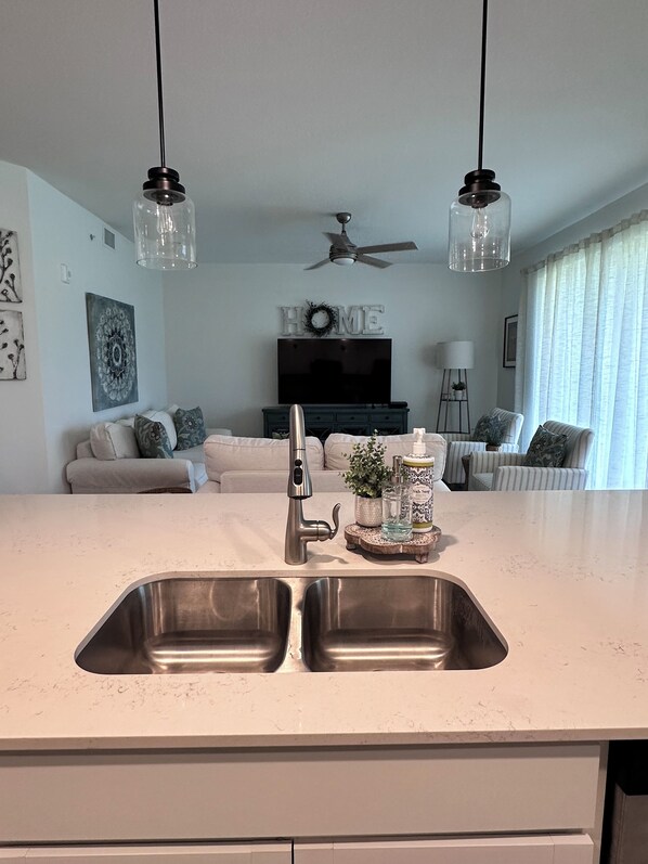 A modern kitchen with a stainless steel sink, a built-in oven, and a dining area with a sofa and chairs.