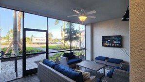 A sunlit patio area with wicker furniture, a ceiling fan, and a view of the street.