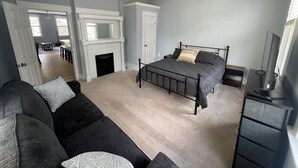 A bedroom with a bed, a ceiling fan, a fireplace, a desk, and a TV.