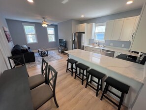 A modern kitchen with a large island, white cabinets, and a dining area with a sofa and chairs. - Central Home 3min to downtown + private parking + 10% off Ark, Aquarium, and Zoo (Covington)