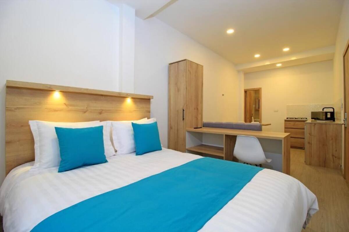 A modern hotel room with a large bed, a desk, and a wardrobe.