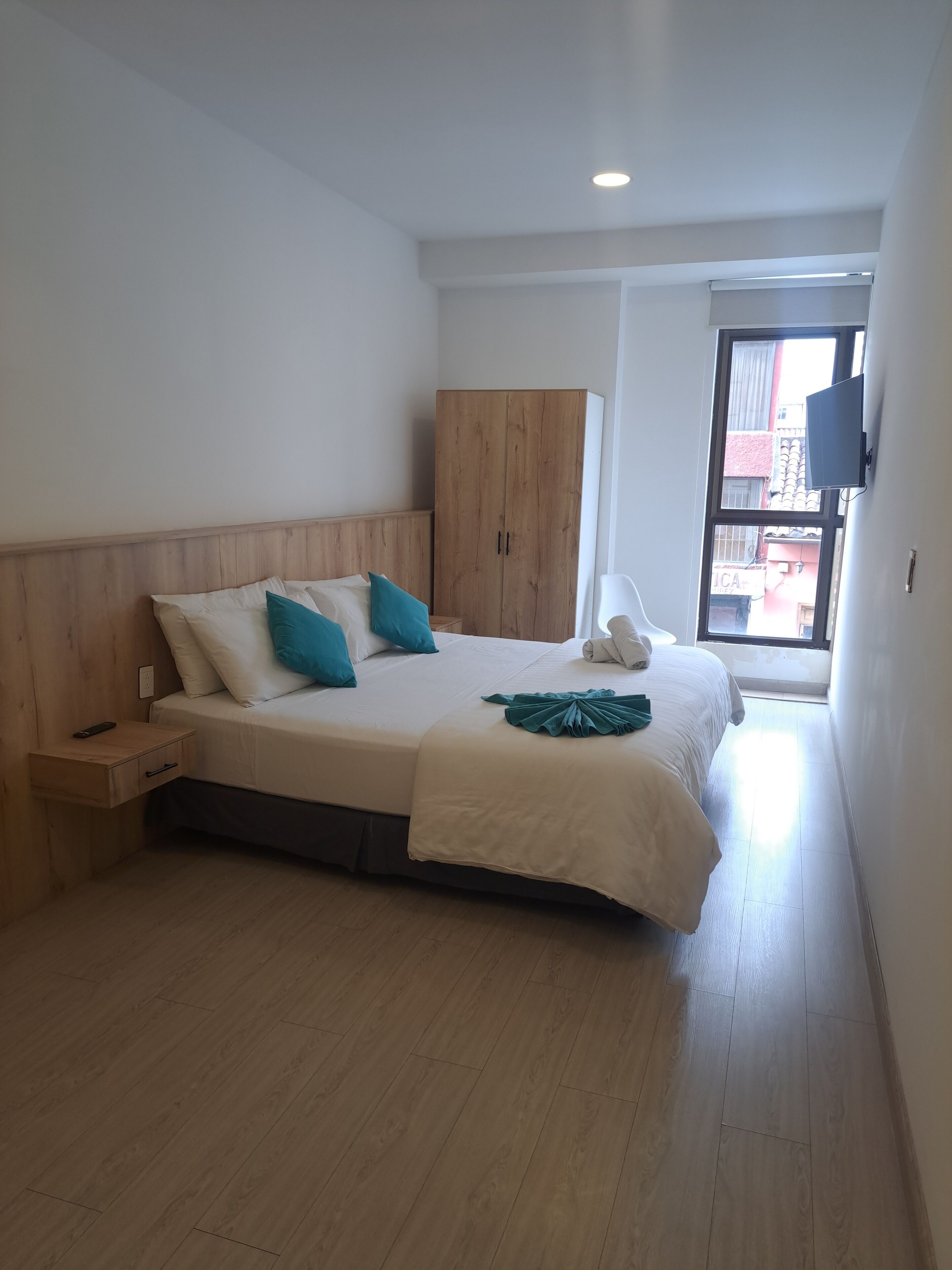 Un dormitorio con cama, armario de madera, mesita de noche y televisor montado en la pared.
