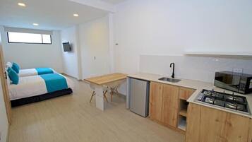 A compact room with a bed, a small kitchenette, and a window.