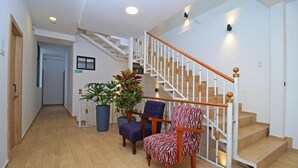 Una escalera con barandillas blancas y escalones de madera, una planta azul en maceta y dos sillas con tapicería estampada.