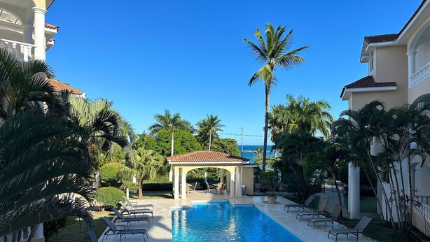 A swimming pool with lounge chairs, a covered seating area, and palm trees. - Oceanfront Penthouse in Puerto Plata (Puerto Plata)